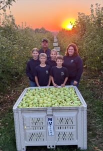 Family in an orchard standing in front of apple bin at sunset.