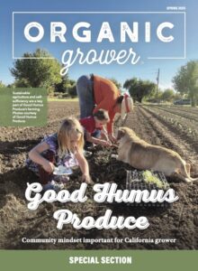 Woman bending over and tending to a farm field while a girl digs in the dirt and a dog lies there.