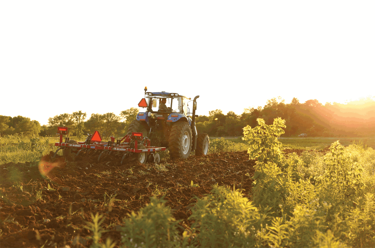 Tractor driving in field at sunset.